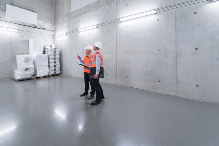 Two colleagues wearing safety vests and hard hats talking in a building